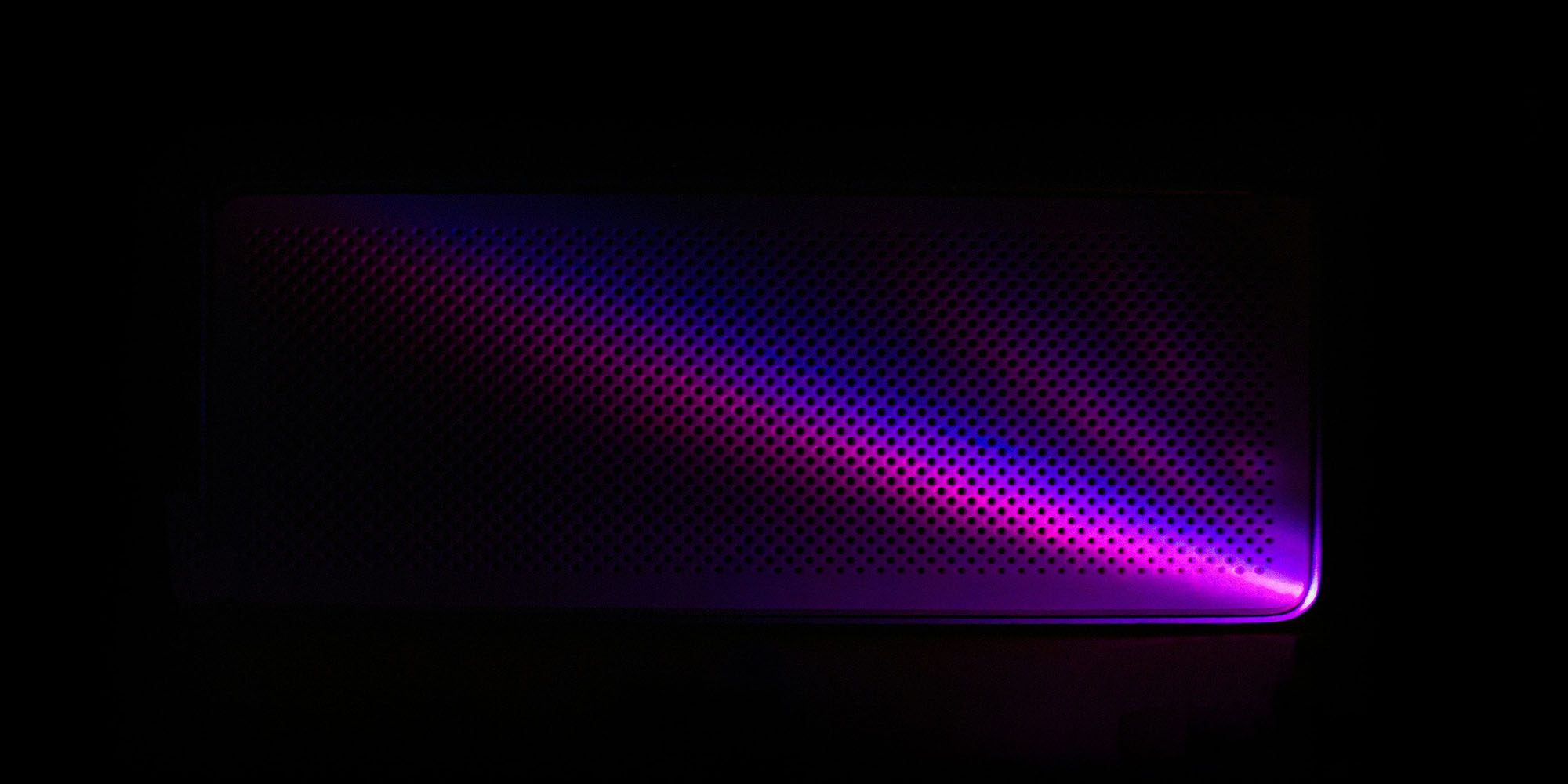 OpenAI's hardware device may partly compete with the upcoming AirPods Ultra | Low key image of a speaker with purple lighting and darkness hiding most of the form factor