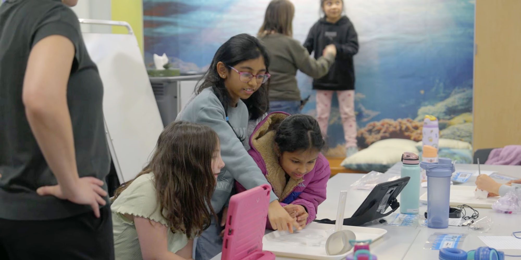 Apple TV doc All of Us shows how iPads enable inclusive learning in a unique school | Photo shows students working together at a large table with the help of two iPads